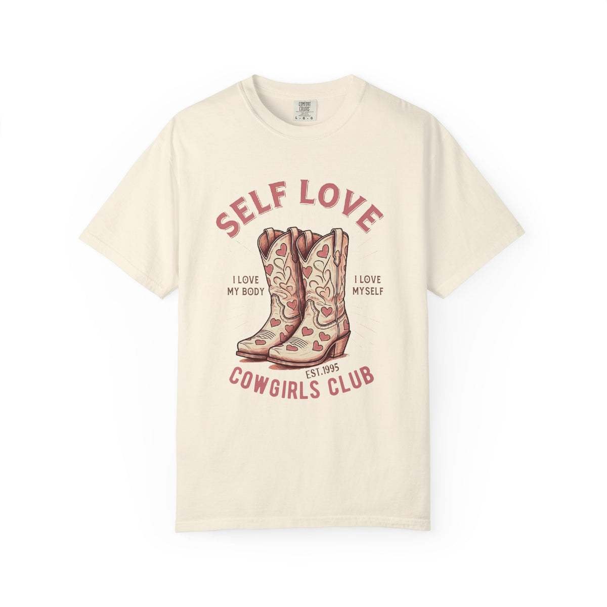 Cream oversized vintage-style t-shirt featuring a graphic of cowgirl boots with pink hearts and the phrase “Self Love Cowgirl Club – I love my body, I love myself.” Western-inspired design with a bold, empowering message.
