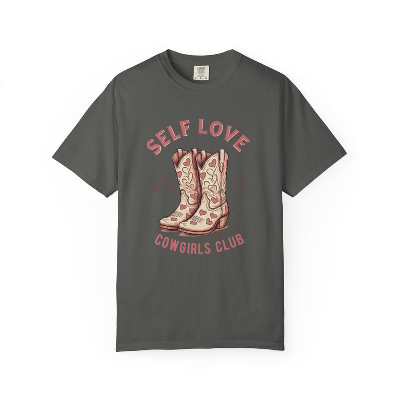Oversized cream t-shirt featuring a graphic of cowgirl boots with pink hearts and the phrase “Self Love Cowgirl Club – I love my body, I love myself.” Western-themed design with empowering self-love messaging.
