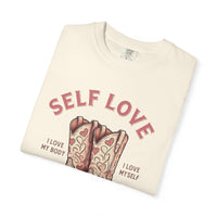 Cream oversized vintage-style t-shirt featuring a graphic of cowgirl boots with pink hearts and the phrase “Self Love Cowgirl Club – I love my body, I love myself.” Western-inspired design with a bold, empowering message.
