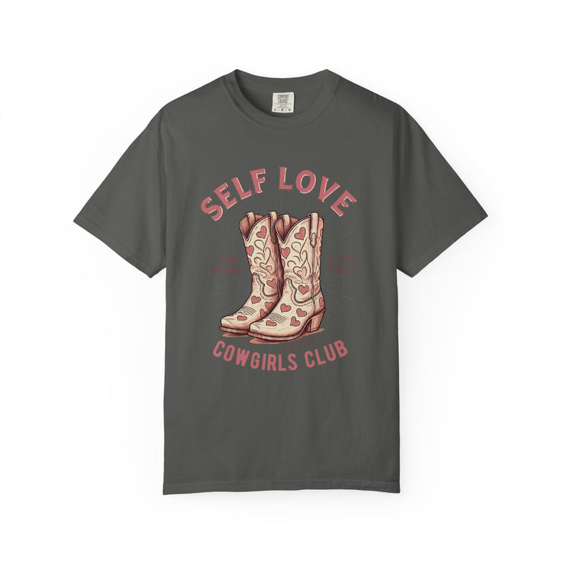 Cream oversized vintage-style t-shirt featuring a graphic of cowgirl boots with pink hearts and the phrase “Self Love Cowgirl Club – I love my body, I love myself.” Western-inspired design with a bold, empowering message.
